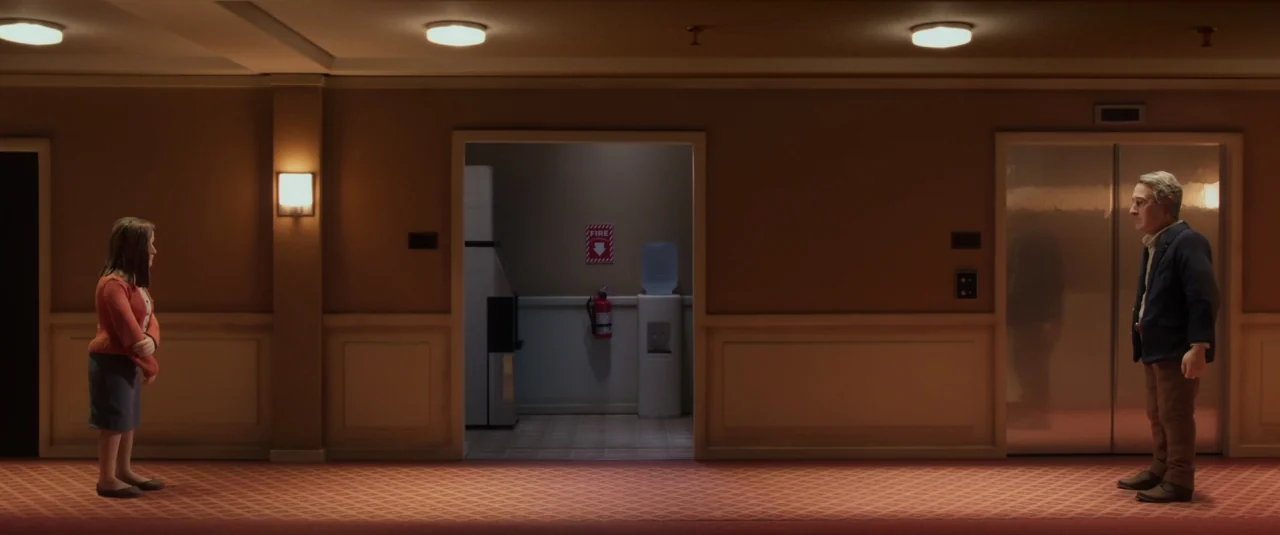 Anomalisa (2015) movie still: wide — A quiet, symmetrical hotel corridor features a carpeted floor and centered elevator doors. A man and a woman…