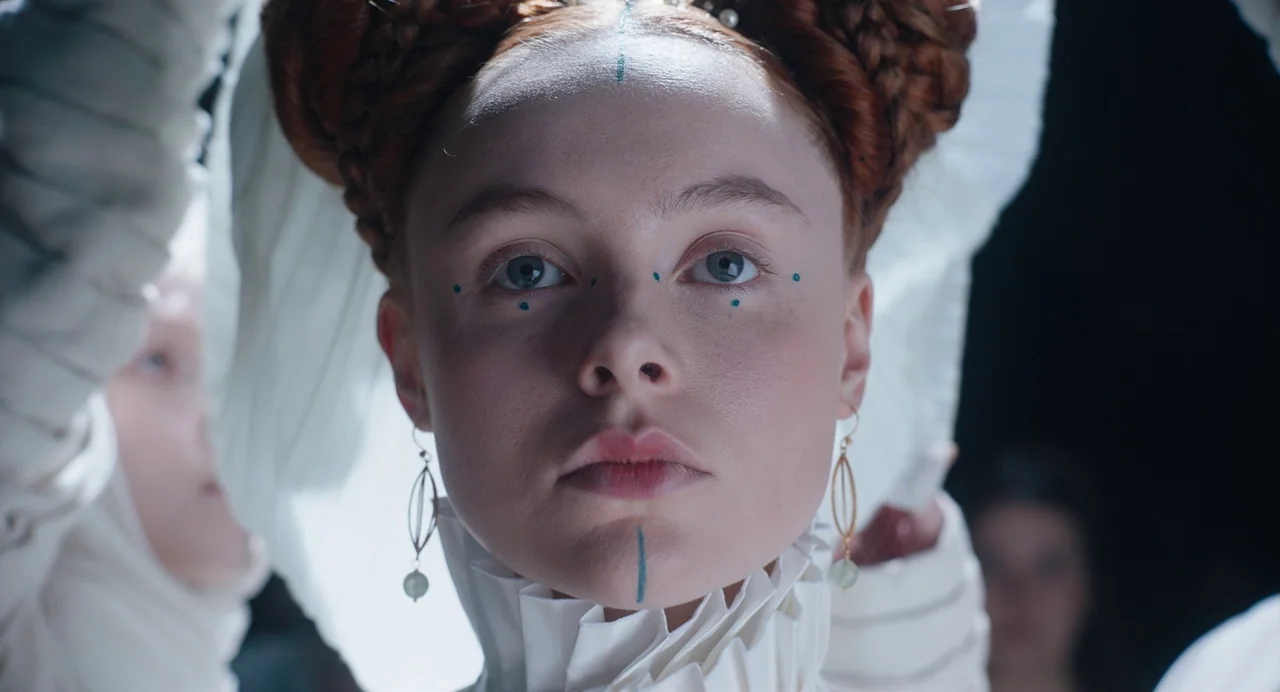 The Green Knight (2021) movie still: closeup — A close portrait of a young woman with complex red braided hair. Her face features minimalist blue…