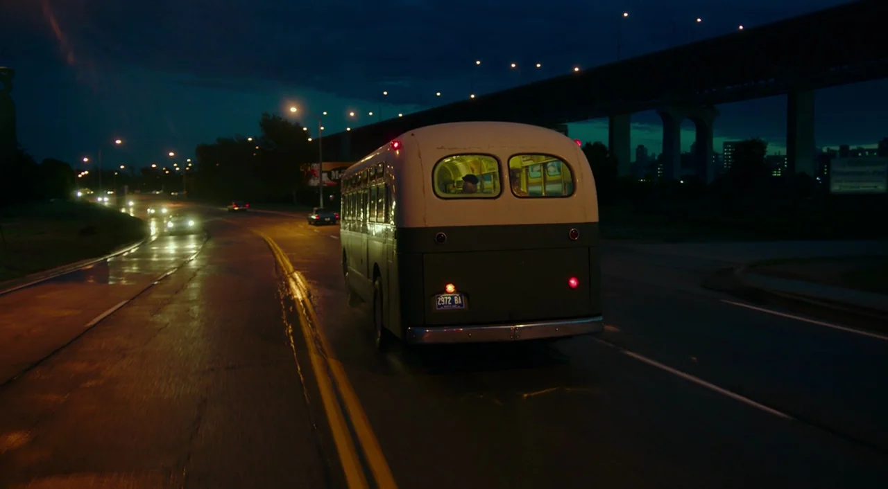 The Shape of Water (2017) movie still: wide — A vintage bus drives along a dark highway at night with a large bridge structure above. The wet…