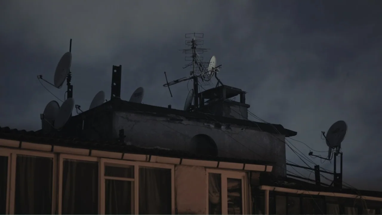 A Gift from God (2019) movie still: establishing — A rooftop surface displays multiple satellite dishes and television antennas against a dark sky.…