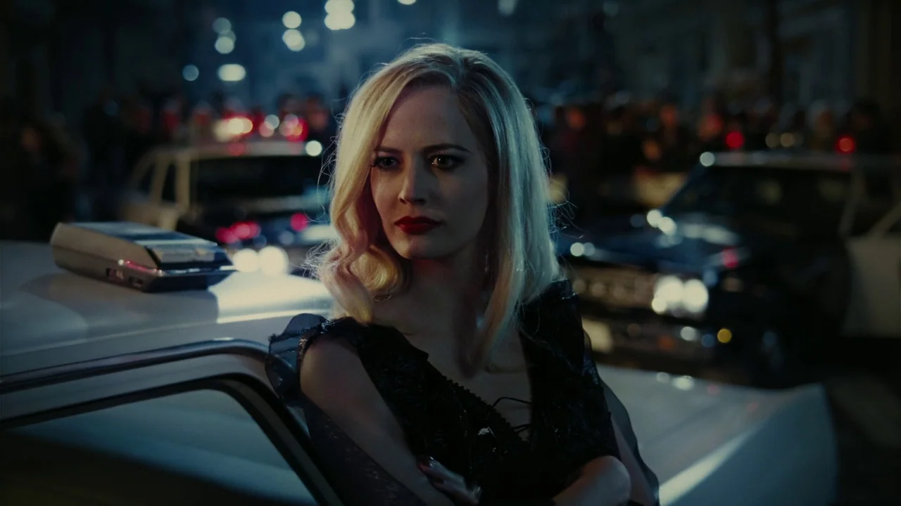Dark Shadows (2012) movie still: medium — A dark urban street at night with blurry police vehicle lights in the background. A blonde woman stands in…