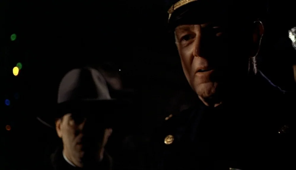 The Godfather (1972) movie still: medium — A night scene featuring two men standing in darkness outside a building. One man wears a police uniform…