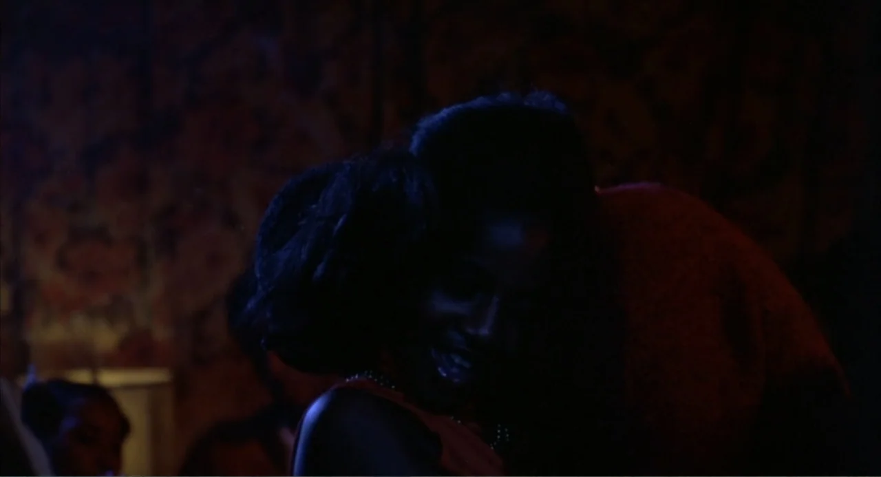 Cooley High (1975) movie still: medium — A dimly lit club interior with textured walls and dark red lighting. A young woman with dark hair and…