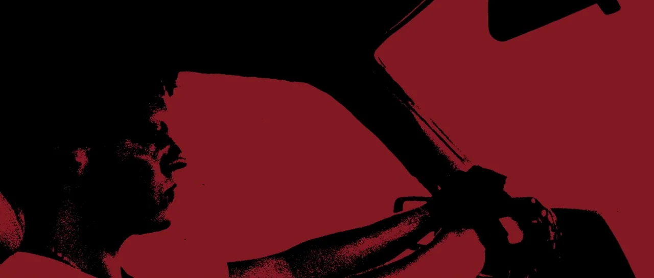 Let The Corpses Tan (2017) movie still: medium — A dark, silhouetted profile of a driver operating a vehicle at night. The driver holds the steering…