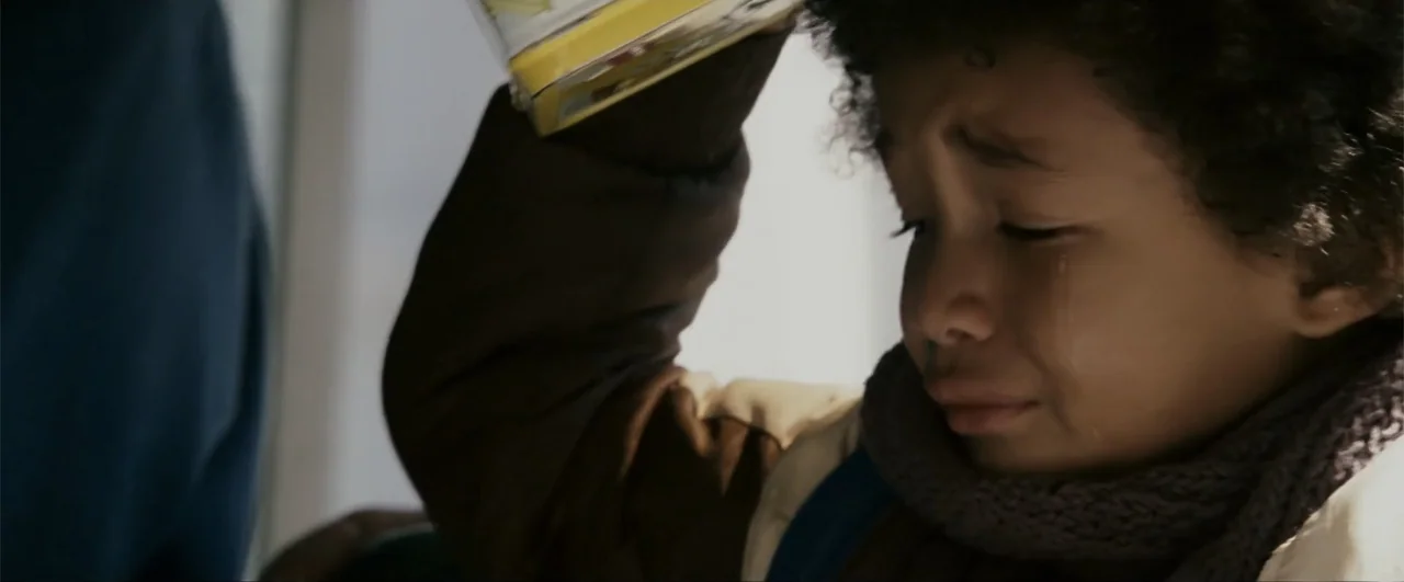 The Pursuit of Happyness (2006) movie still: closeup — A close-up view of a child inside a domestic space. The child holds a plastic container over…