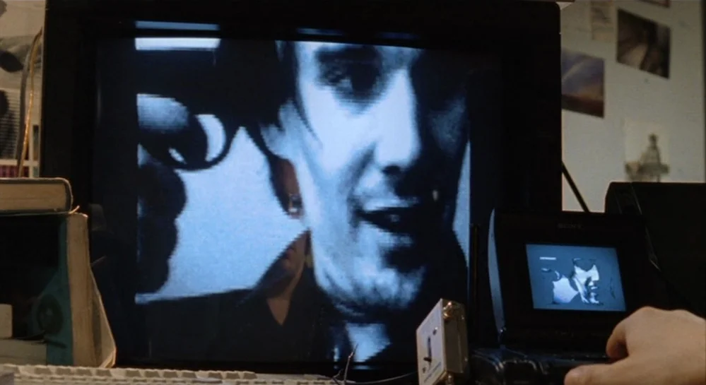 Hamlet (2000) movie still: medium — A dimly lit workstation features a large television monitor displaying a grainy video feed. A man on the screen…