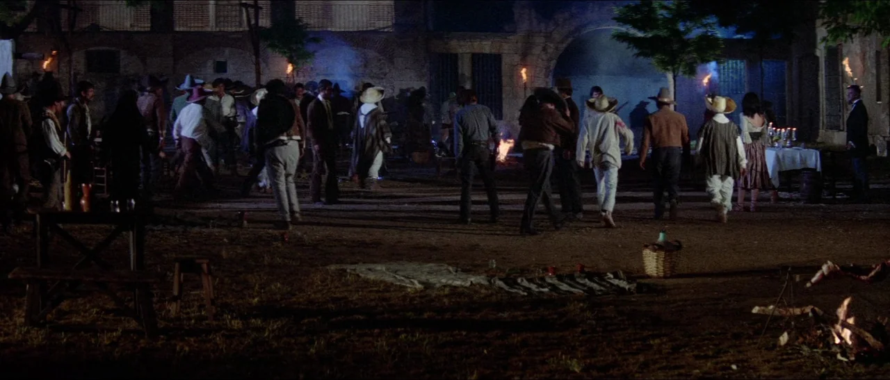 Texas, Adios (1966) movie still: wide — A nighttime outdoor gathering takes place in a dirt-floored plaza near stone buildings. Numerous figures…