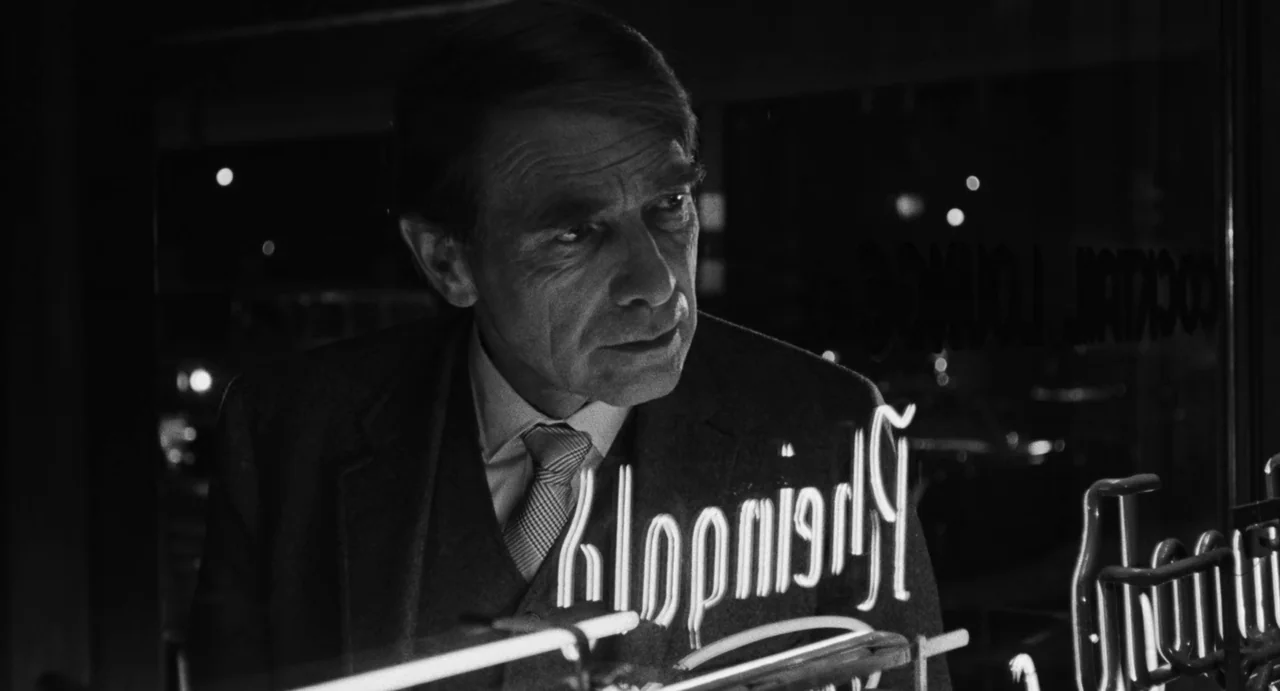 The Incident (1967) movie still: closeup — A man stands outside a storefront window at night near an illuminated neon sign. The bright light…