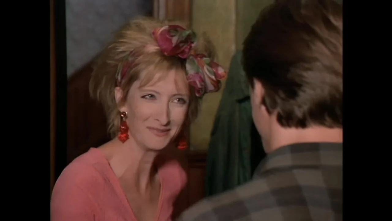 The Awakening (1995) movie still: medium — A domestic interior with a woman wearing a floral hairpiece facing a man. The man is seen from behind in…