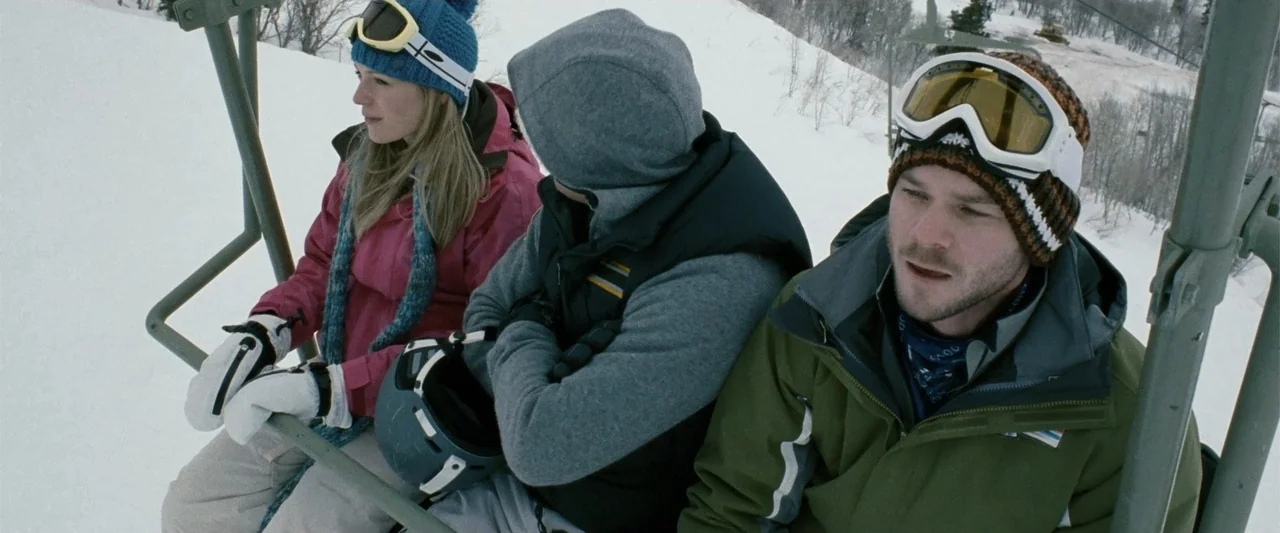 Frozen (2010) movie still: medium — Three people sit on a ski lift moving over a snowy mountain slope. They wear winter sports gear including…