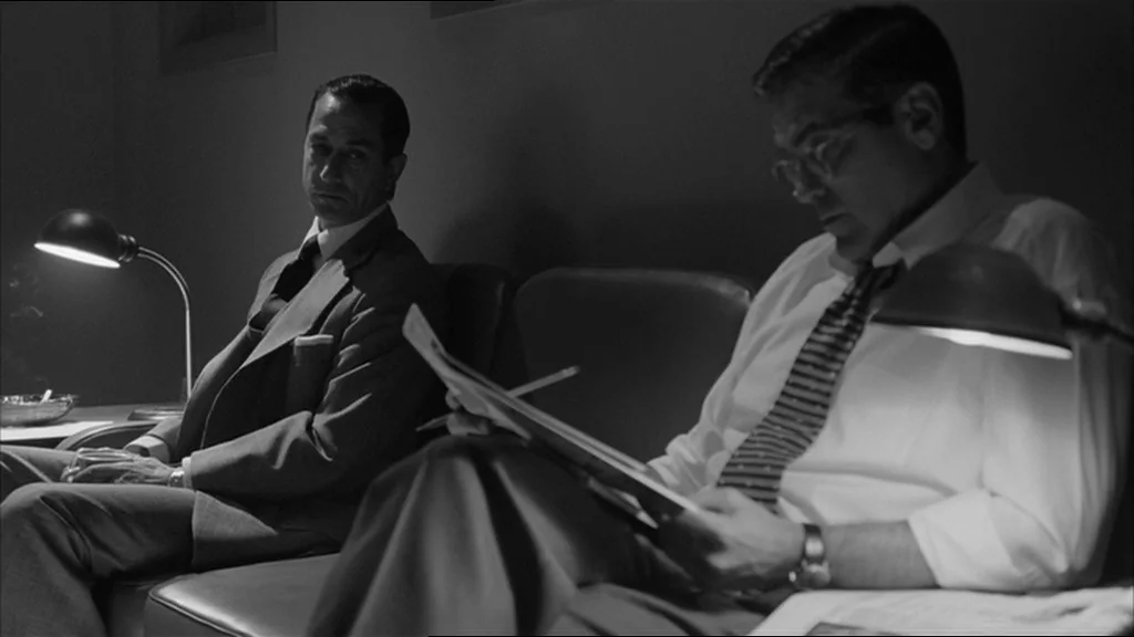 Good Night And Good Luck (2005) movie still: medium — A dimly lit room features two men seated on a bench beneath individual lamps. The two men sit…