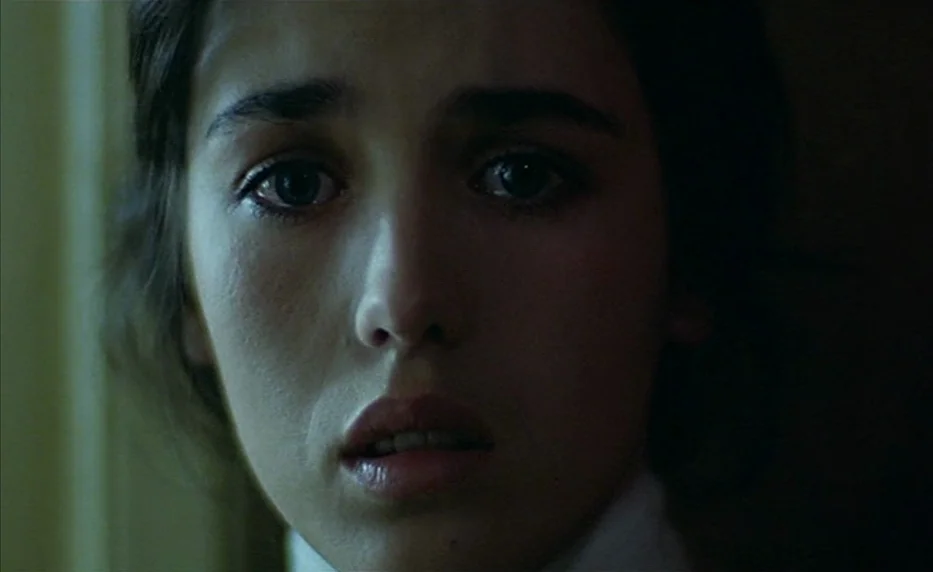 Possession (1981) movie still: closeup — A dimly lit room provides the backdrop for a close-up of a young woman. She faces forward with her gaze…