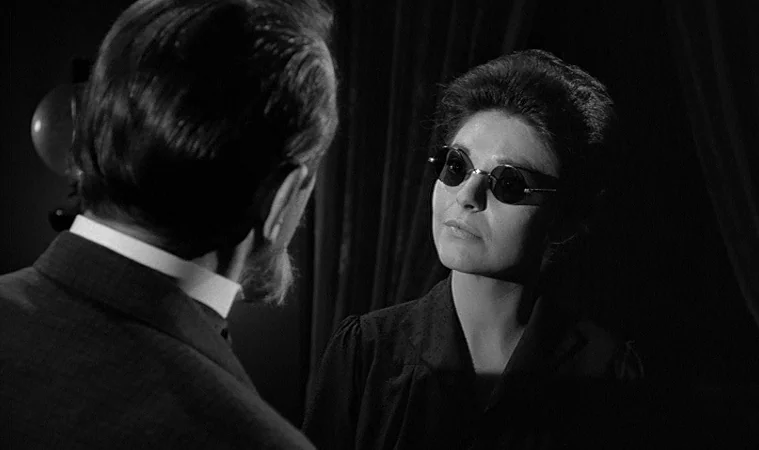 The Miracle Worker (1962) movie still: medium — A dimly lit indoor space with heavy curtains visible in the background shadows. A woman wearing dark…