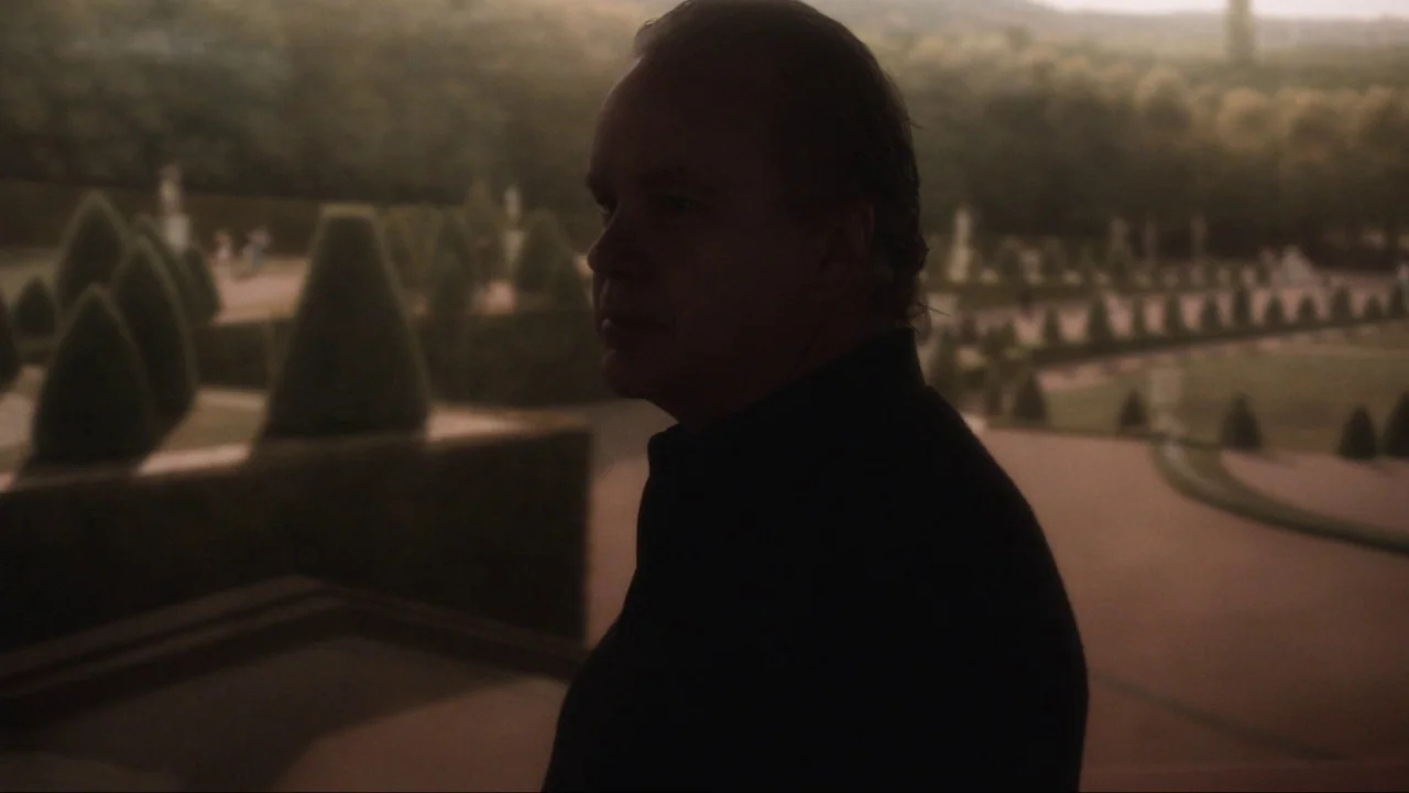 Marjorie Prime (2017) movie still: medium — A man stands on a stone balcony overlooking a formal landscaped garden with topiary. He is silhouetted…