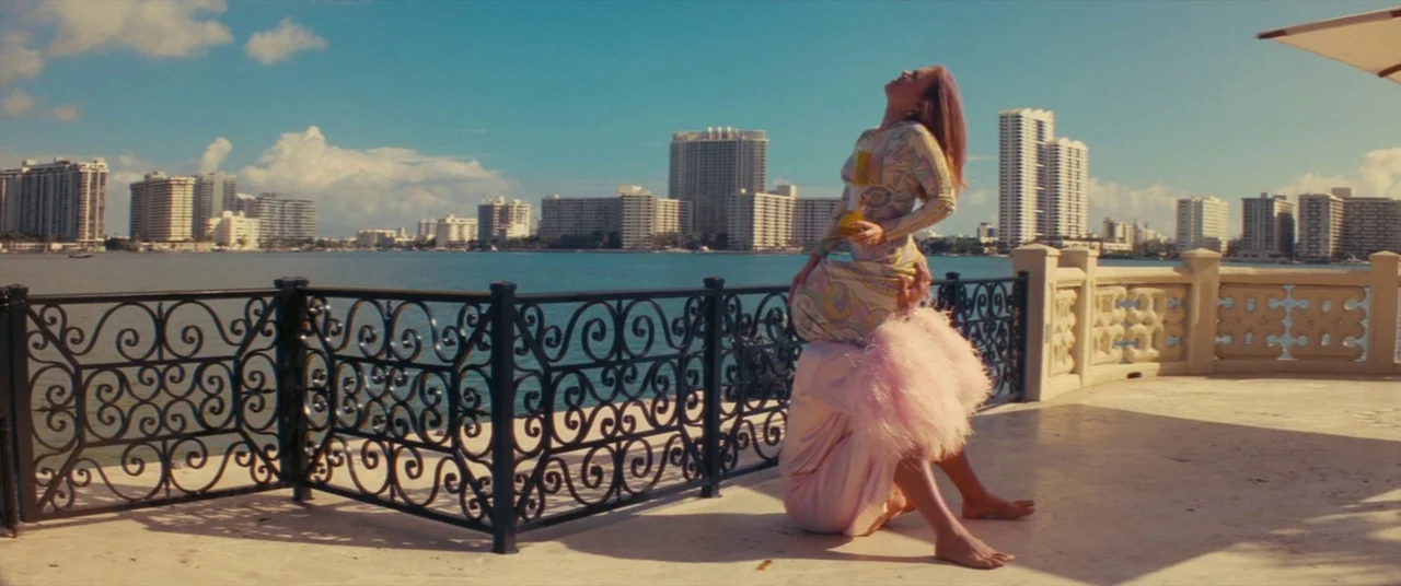 The Beach Bum (2019) movie still: fullbody — A waterfront balcony overlooking a bay with a city skyline in the distance. A woman sits on another…