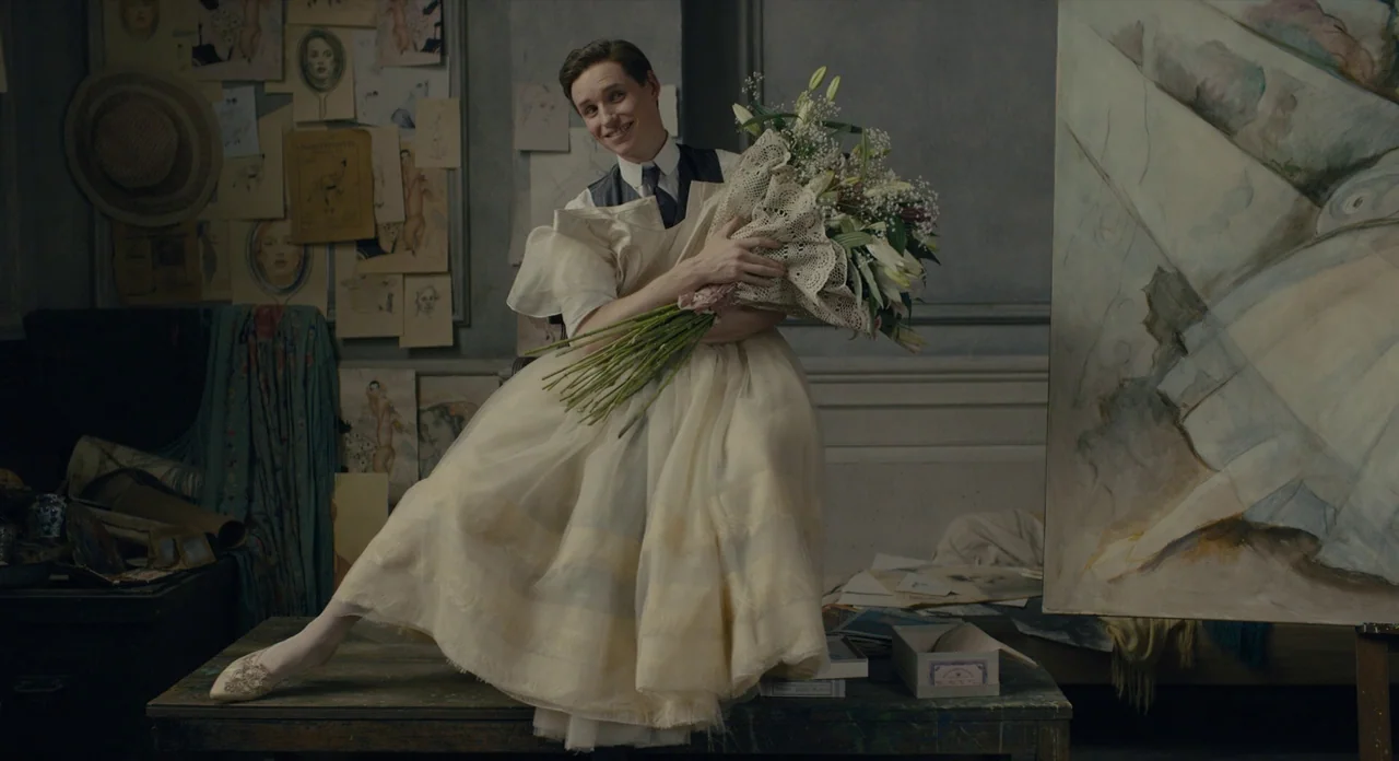 The Danish Girl (2015) movie still: medium — A cluttered art studio features sketches pinned to walls and an easel with canvas. A person wearing a…