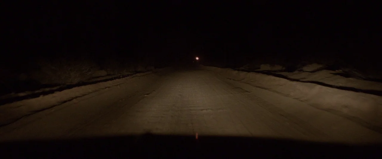 Southbound (2015) movie still: wide — A dark, unpaved road at night stretches forward into the blackness. The path is flanked by low dirt berms and…