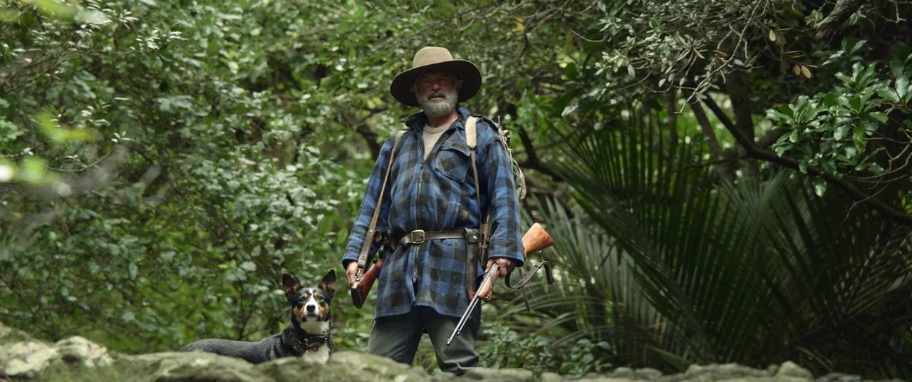 Hunt for the Wilderpeople (2016) movie still: fullbody — A dense subtropical forest with thick green vegetation and large palm fronds. A man in a…