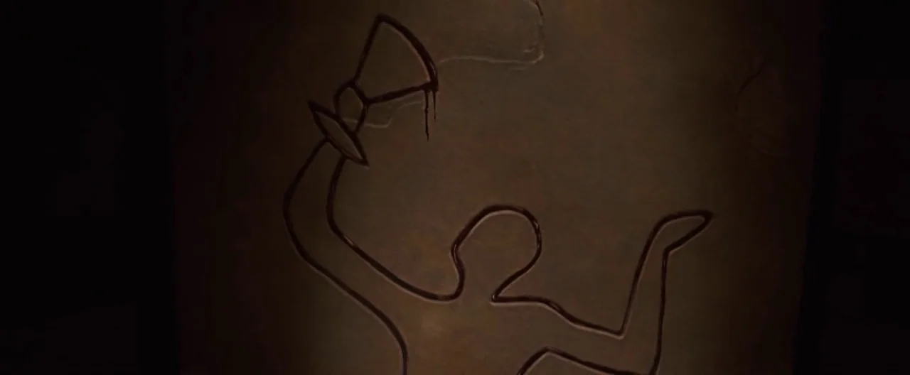 The Cabin In The Woods (2012) movie still: closeup — A dark stone surface features an etched outline of a human figure. The etched shape holds a…