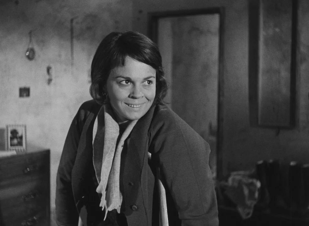 Il Bidone (1955) movie still: medium — A sparsely decorated room with a textured wall and a doorway in the background. A woman leans forward…
