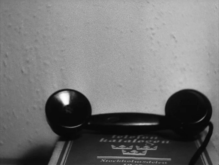 To Joy (1950) movie still: closeup — A close view of a black telephone handset resting on a vintage directory. The textured wall provides a neutral…