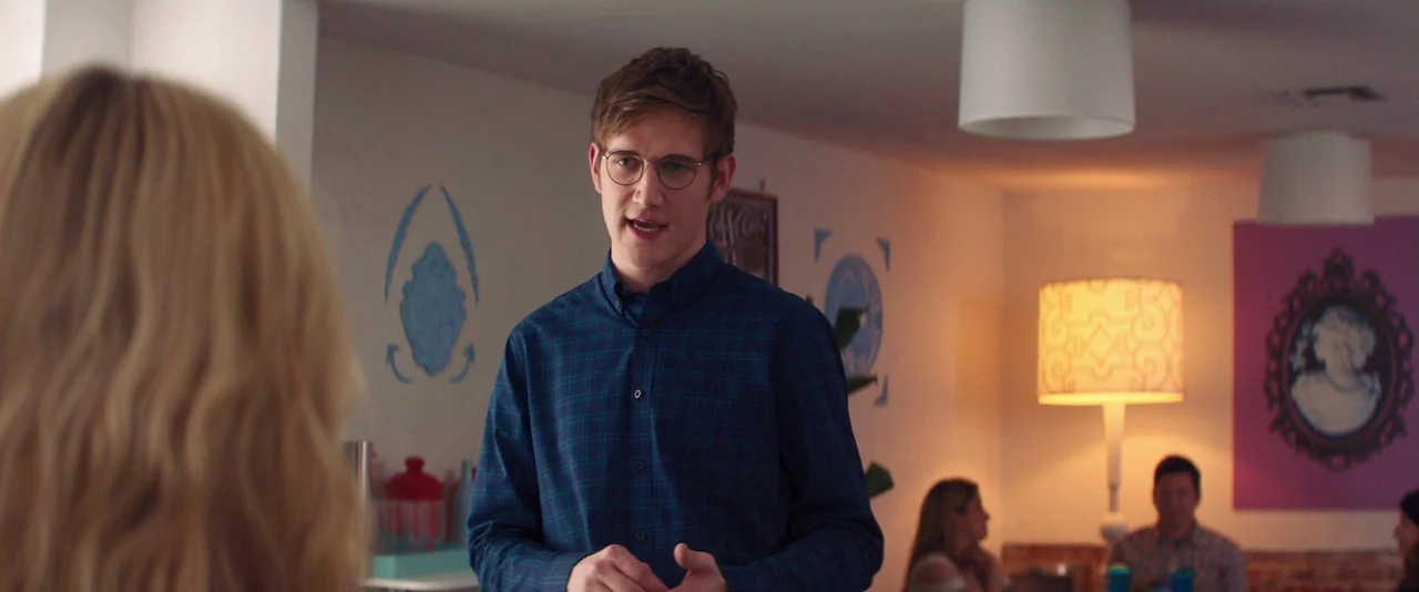 Promising Young Woman (2020) movie still: medium — A well-lit cafe interior features white walls decorated with blue stencil paintings and pink art.…