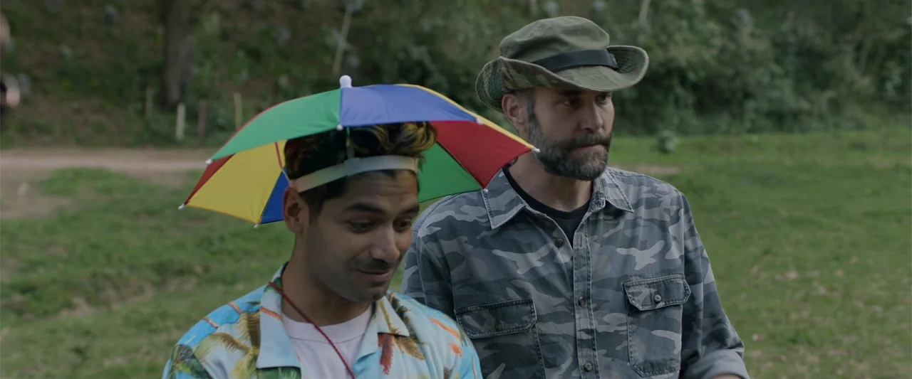 Mirreyes contra Godínez 2: El retiro (2022) movie still: medium — A grassy outdoor area with trees visible in the soft-focus background. Two men…