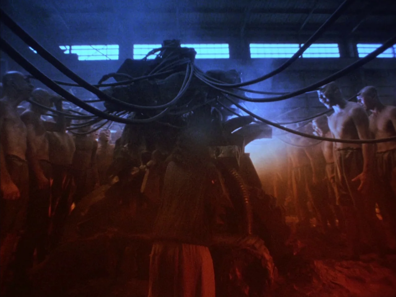 Tetsuo II: Body Hammer (1992) movie still: wide — An industrial hall with high windows and a central machine linked by heavy cabling. A group of…
