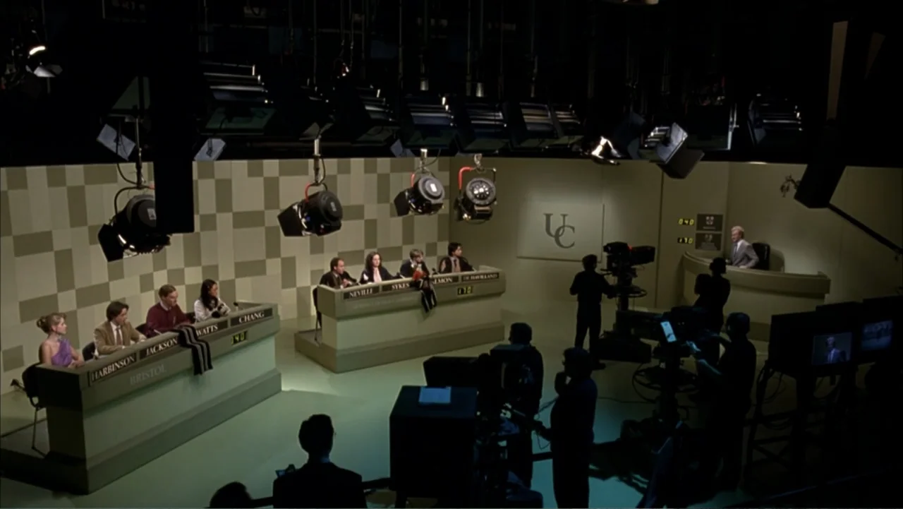 Starter for 10 (2006) movie still: wide — A television quiz show set features two long desks for students and equipment overhead. A group of…