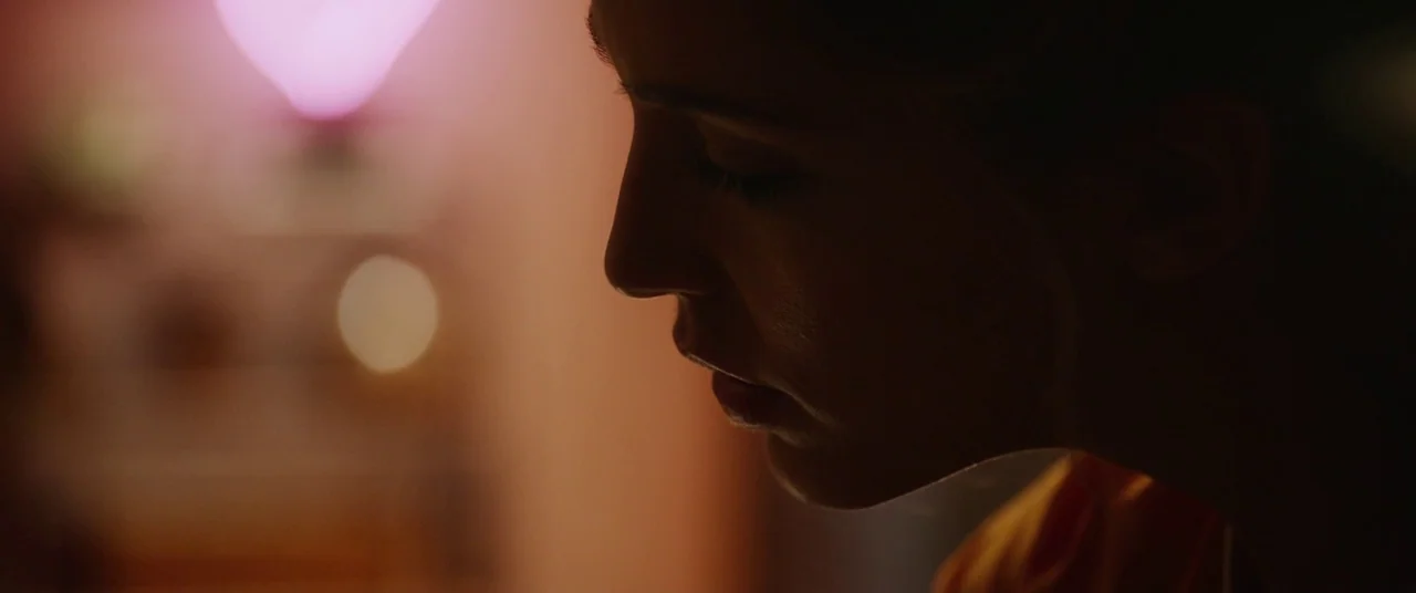 Happy Death Day (2017) movie still: closeup — The side of a woman's face is lit against a dark background with bokeh lights. She gazes downward…