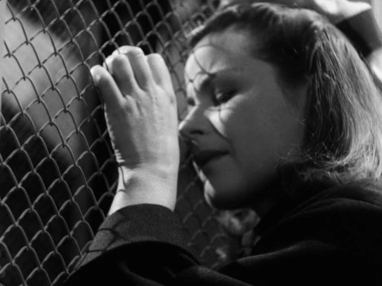 Waiting Women (1952) movie still: closeup — A close-up shot of a person standing directly behind a wire mesh fence. The subject leans her head and…