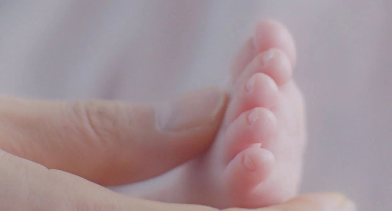 Train To Busan movie still: closeup — A soft-focus view shows a person holding the small foot of an infant. The pale, smooth skin of the baby is…