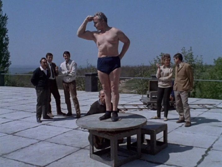 Innocence Unprotected (1968) movie still: fullbody — A flat stone terrace overlooks a distant landscape under a clear sky. A man on a low pedestal…