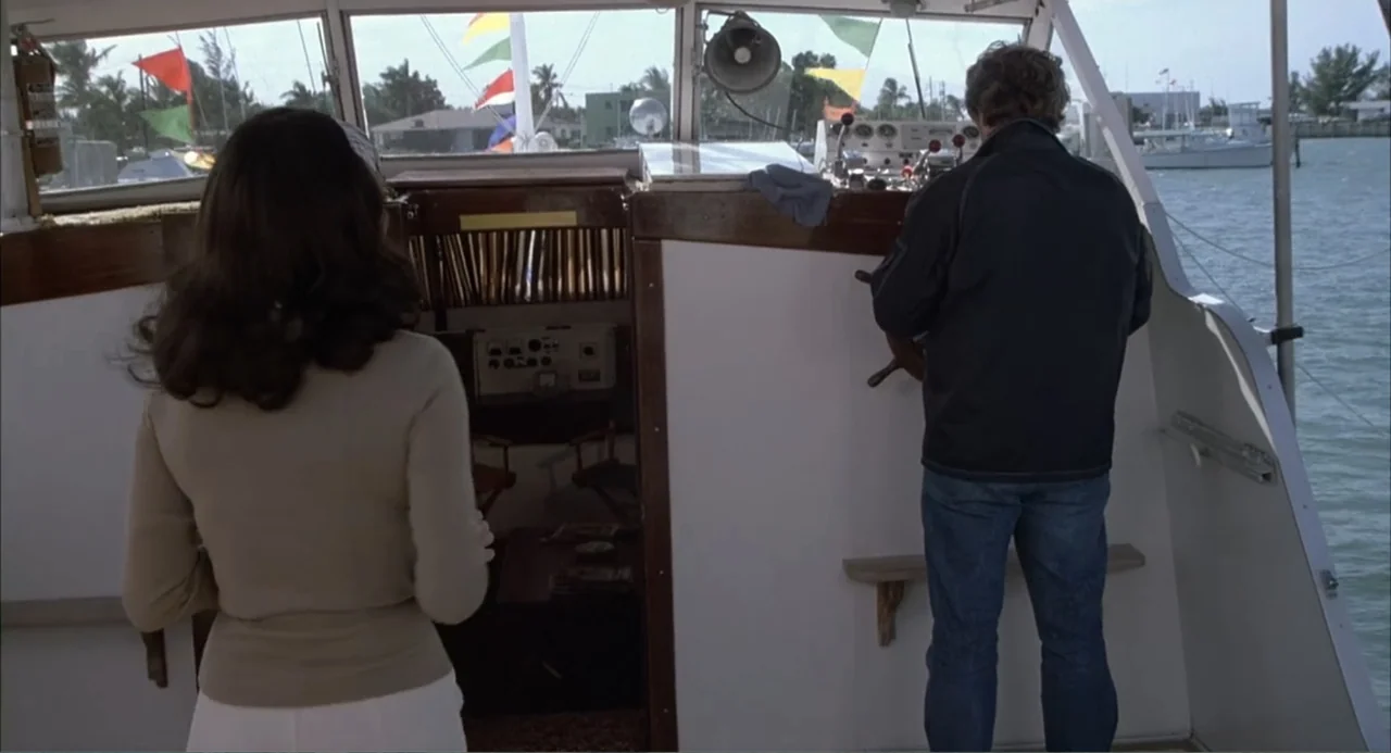 Empire of the Ants (1977) movie still: fullbody — A boat cabin features white paneling, wooden door frames, and a helm station. A man steers the…