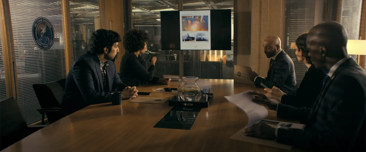 The Beekeeper (2024) movie still: wide — A modern office conference room features wood-paneled walls and a long polished table. Five professionals…