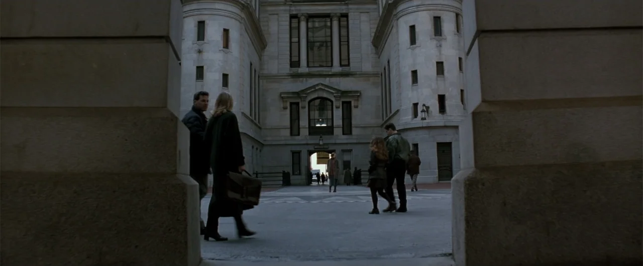 Fallen (2004) movie still: wide — A stone-walled courtyard with arched entrances connects classical building facades under overcast skies. Several…
