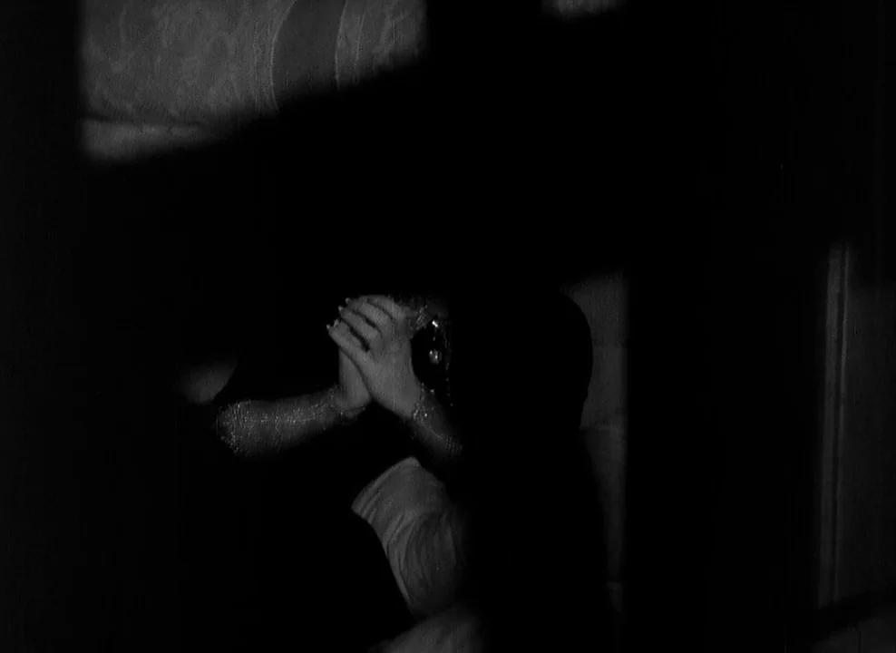 Shanghai Express (1932) movie still: closeup — A darkened interior space features a person with hands clasped near their face. The figure is largely…