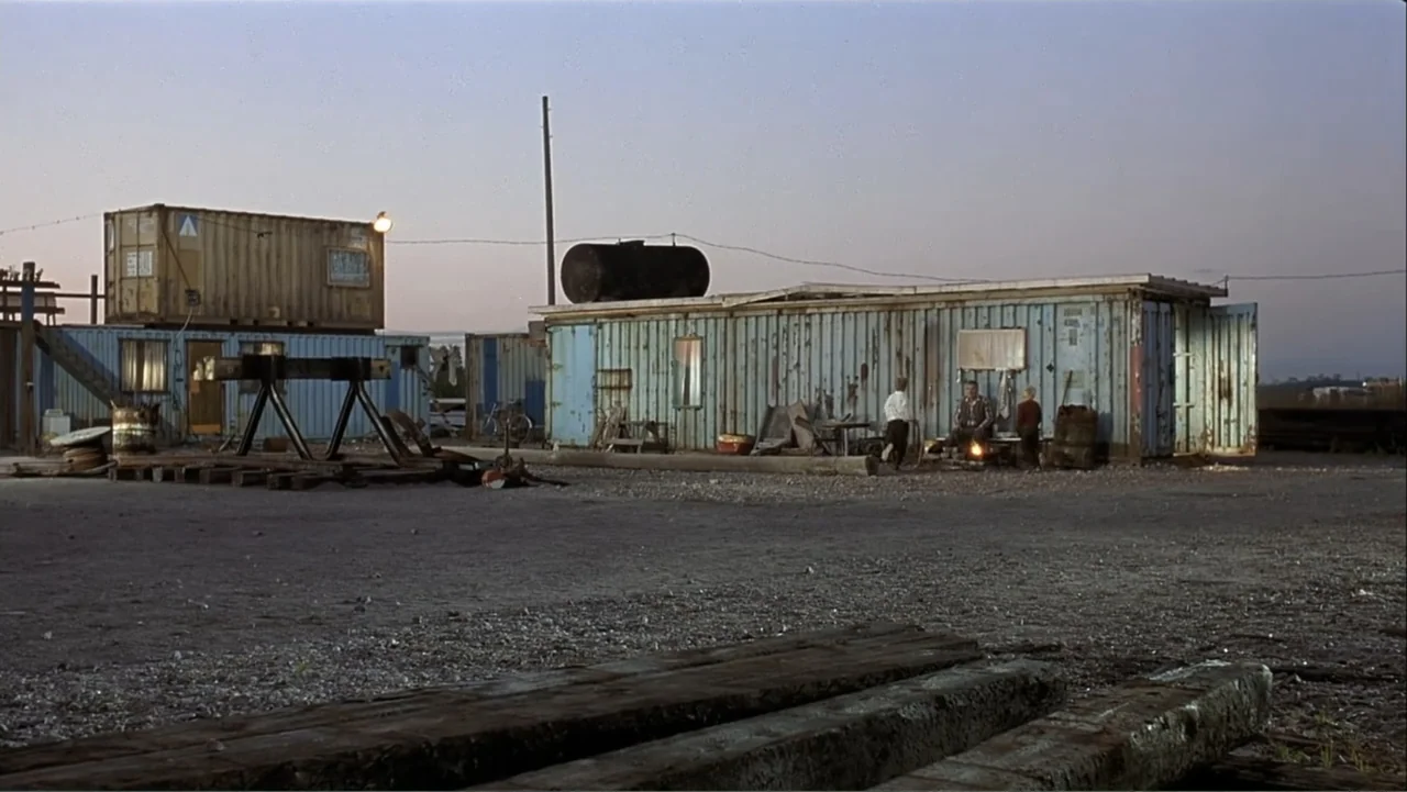 The Man Without a Past (2002) movie still: wide — An industrial outdoor yard features weathered blue and tan shipping containers arranged on gravel…