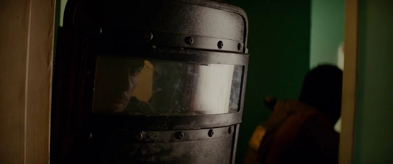 Triple 9 (2016) movie still: closeup — A dark, cramped interior space features a green-walled passage illuminated by dim ambient light. A tactical…
