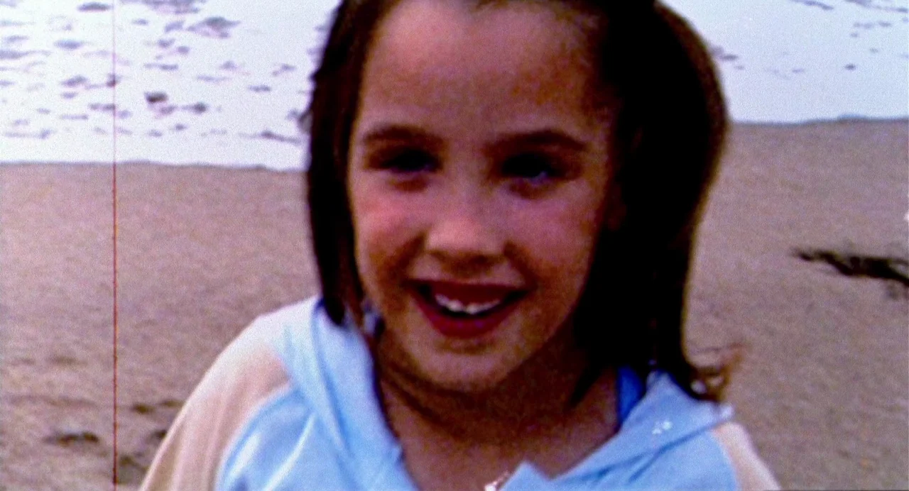 The Nameless (1999) movie still: closeup — A young girl smiles at the camera on a sandy beach. Waves are visible behind her as she stands near the…