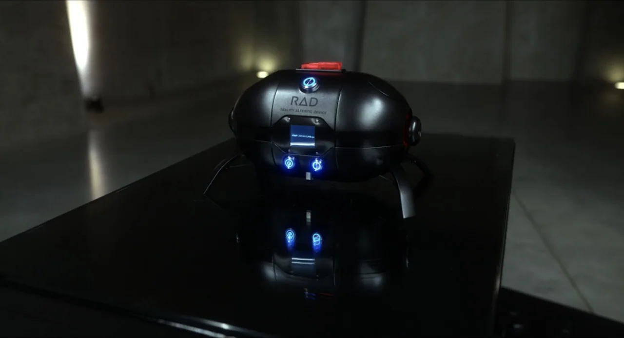 Henry Danger: The Movie (2025) movie still: closeup — A dark, industrial-style space contains a glossy black pedestal. A compact, rounded metallic…