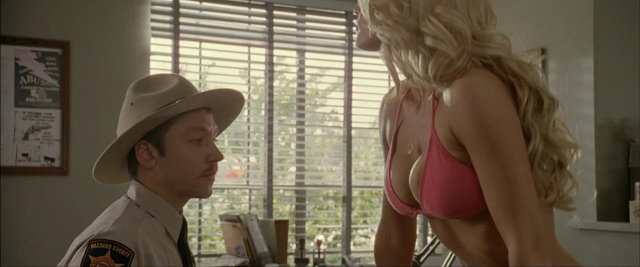 The Dukes of Hazzard (2005) movie still: medium — A light-walled office contains a desk and a window with closed horizontal blinds. A woman in a…