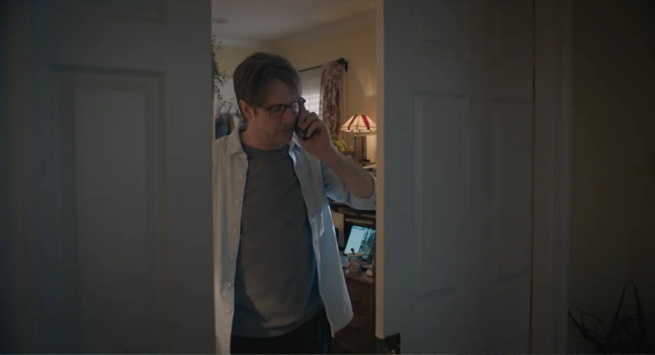 The Map of Tiny Perfect Things (2021) movie still: medium — A man in a light blue shirt stands framed within an open white doorway. He holds a black…