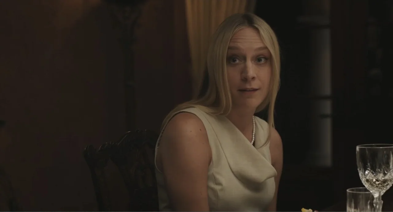 Beatriz at Dinner (2017) movie still: medium — A dimly lit dining room features dark wood furniture and minimal background decor. A woman sits at a…
