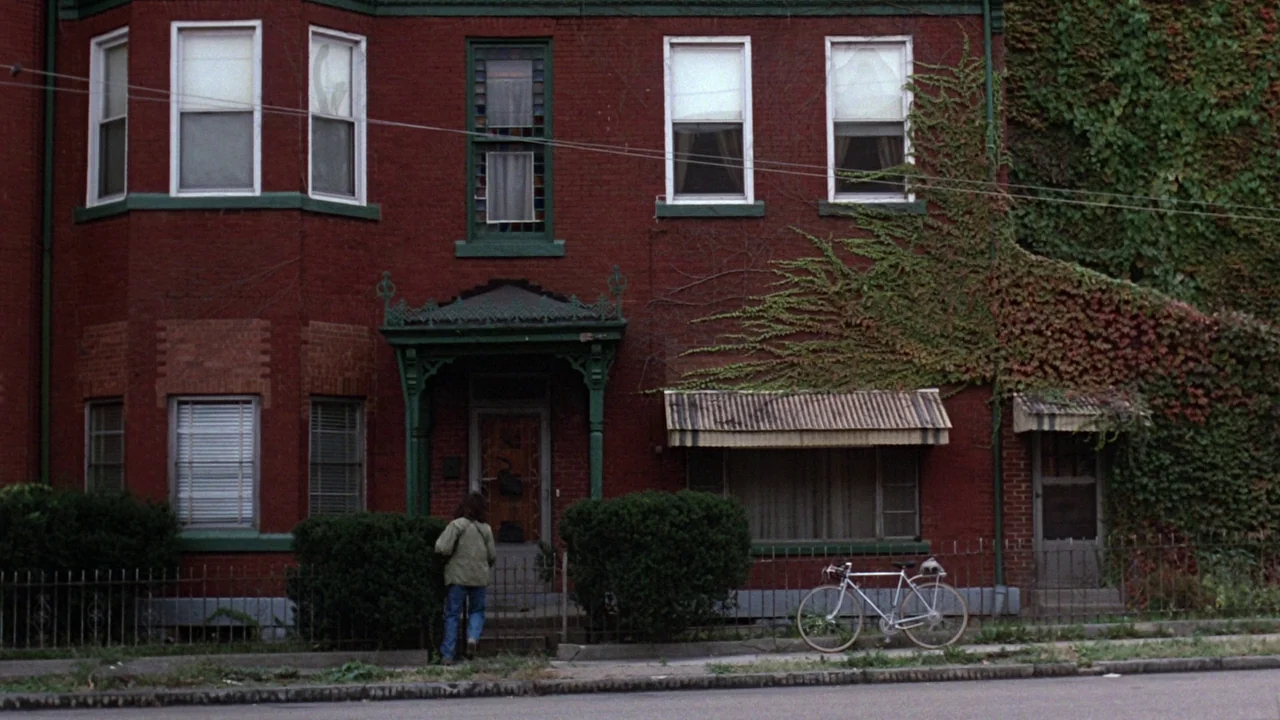 Flashdance (1983) movie still: wide — A three-story red brick row house features green trim and ivy covering one side. A person stands before the…