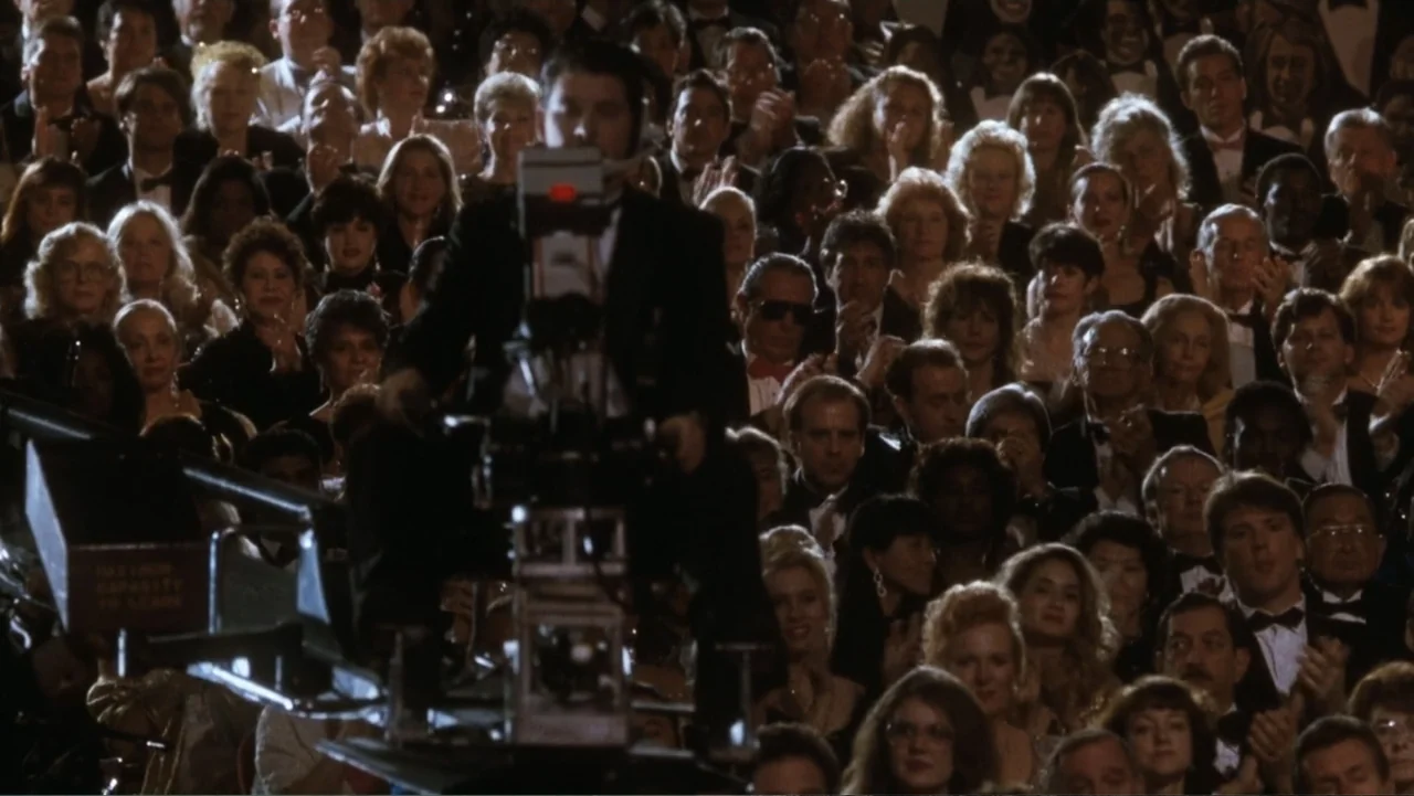 The Bodyguard (1992) movie still: medium — A crowded auditorium filled with people in formal evening wear clapping at an event. A camera operator…