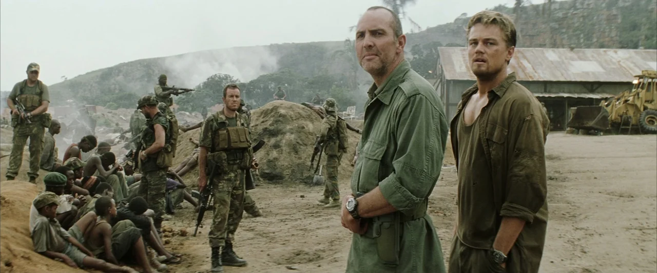 Blood Diamond (2006) movie still: medium — A dusty military camp with several armed soldiers standing near piles of dirt. Two men in the foreground…