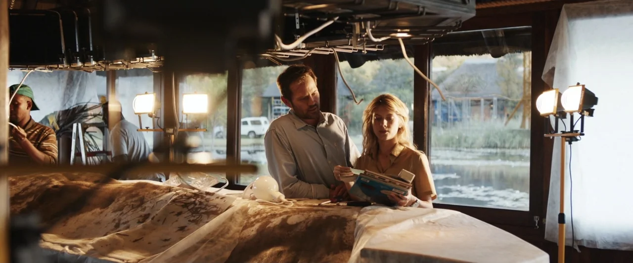 Mia and the White Lion (2018) movie still: medium — A rustic wood-paneled room features large windows overlooking a calm outdoor pond area. A man…
