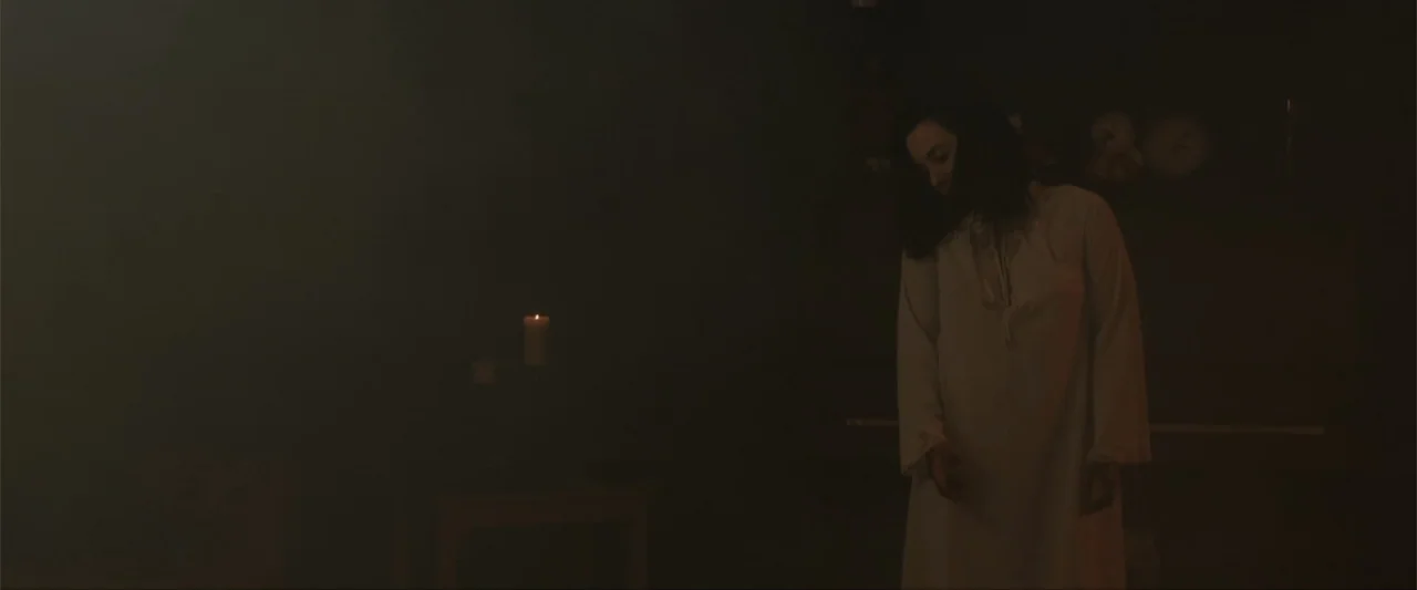 Anomaly (2006) movie still: medium — A dimly lit, hazy interior space is filled with thick, low-hanging smoke. A young woman in a white nightgown…