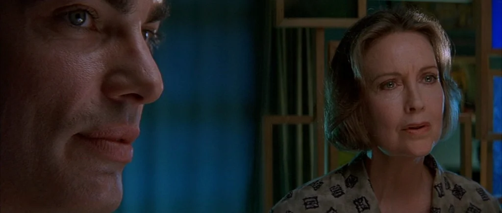 The Underneath (1995) movie still: medium — A dimly lit interior space features blue curtains and a decorative wooden grid background. A middle-aged…